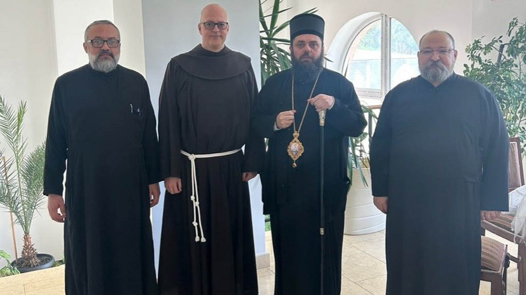 Four clergymen in black robes posing indoors; the third wears a bishop's hat and ornate cross.