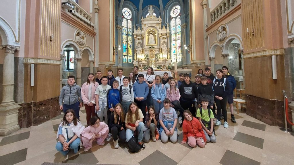 Group of children and a few adults posing inside a grand church, with a gilded altar and stained-glass windows behind them.