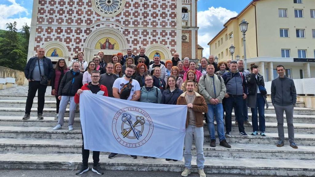 Large group of people posing on church steps behind a light blue banner with a circular emblem.