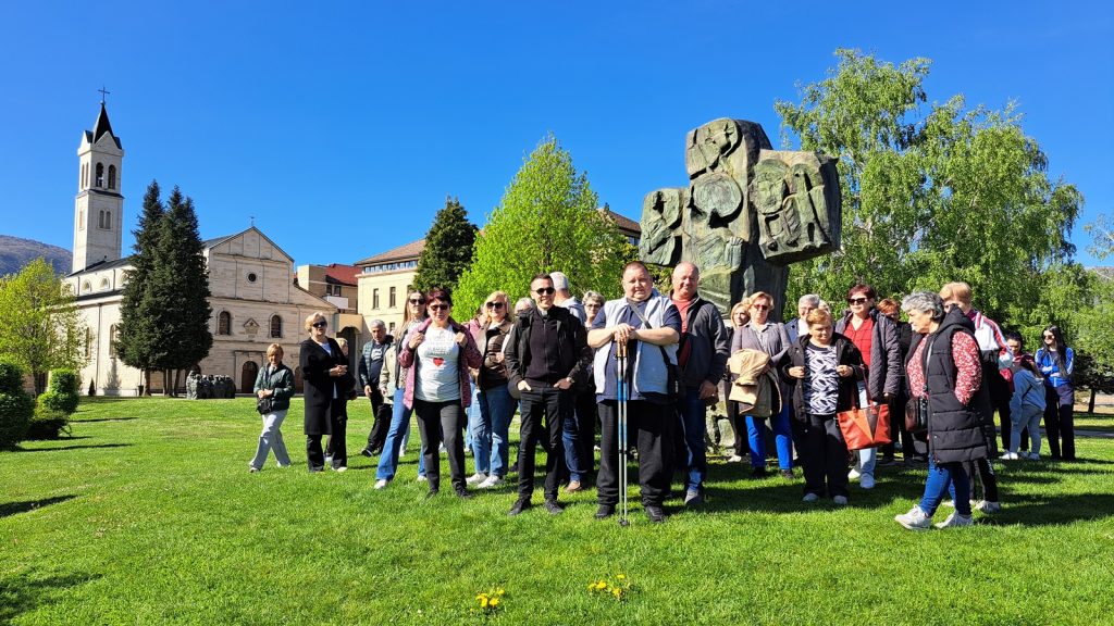 Group of people posing on a sunny lawn beside a large stone sculpture, with a church and trees in the background.