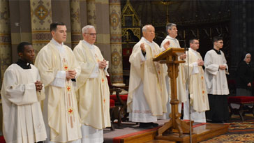 Group of Catholic priests in white vestments standing on a church platform during a ceremony.