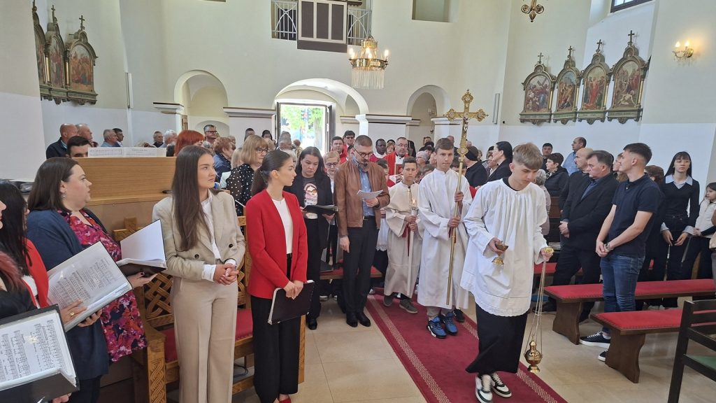Church interior during a service with a procession; altar servers in white robes and a priest holding a censer leads the group.