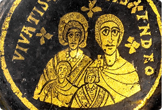 Gold circular medallion featuring two adult figures and two children, bordered by Latin inscription around the edge.