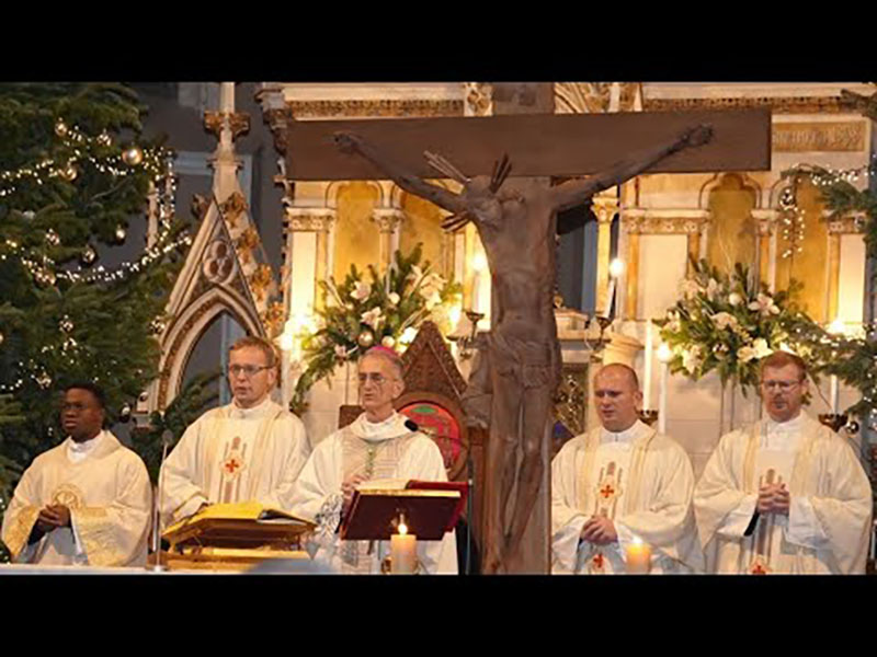 Priests in white vestments standing at an altar with a crucifix during a Christmas church service.