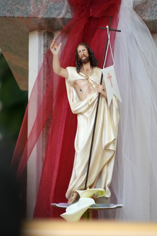 Statue of Jesus Christ in a white robe, raising his right hand, holding a cross staff in a procession display.