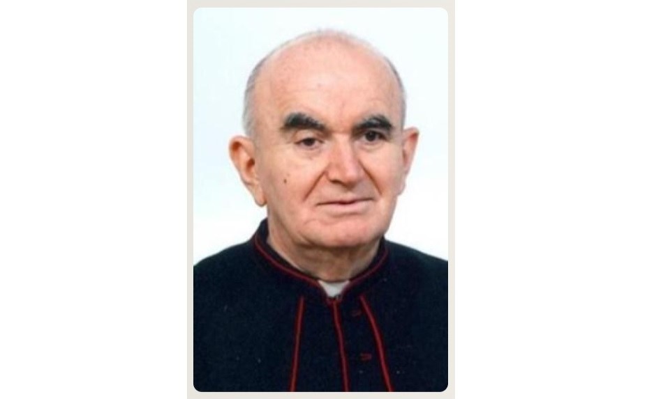 Close-up portrait of an older man in a black clerical robe with red piping.