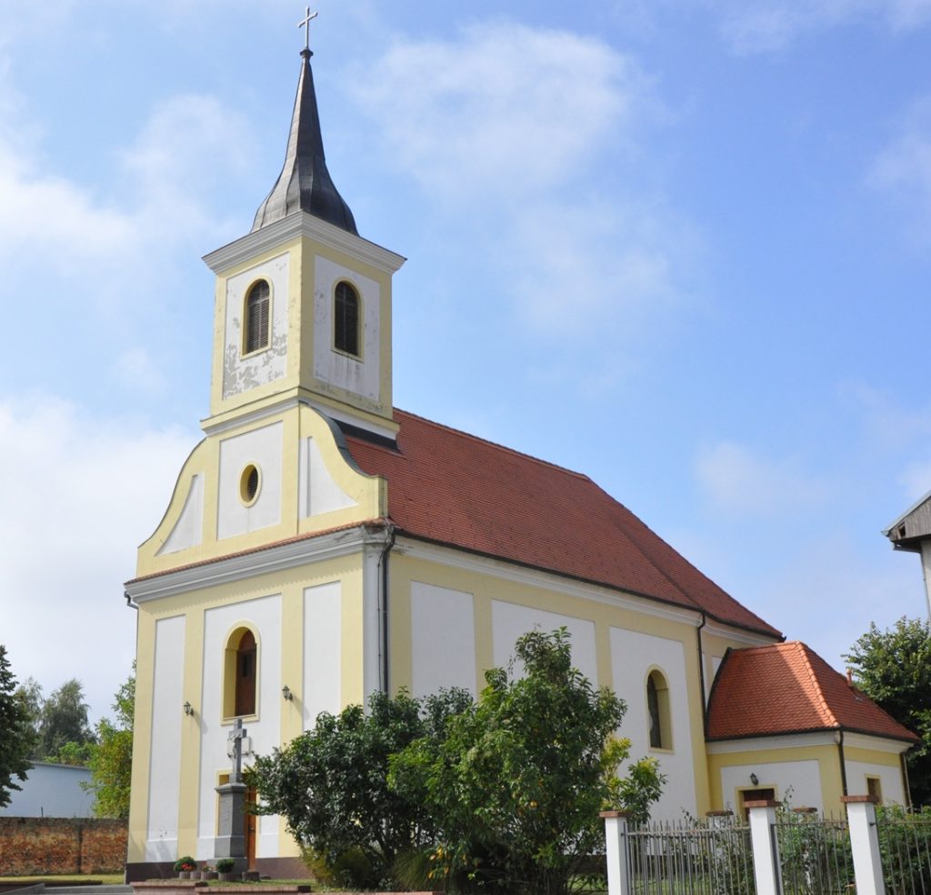 Small church with yellow and white exterior, steep steeple, and cross against a blue sky