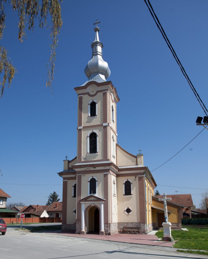 Front view of a tall church with pale pink walls and arched windows under a clear blue sky, topped by a silver onion dome and cross.