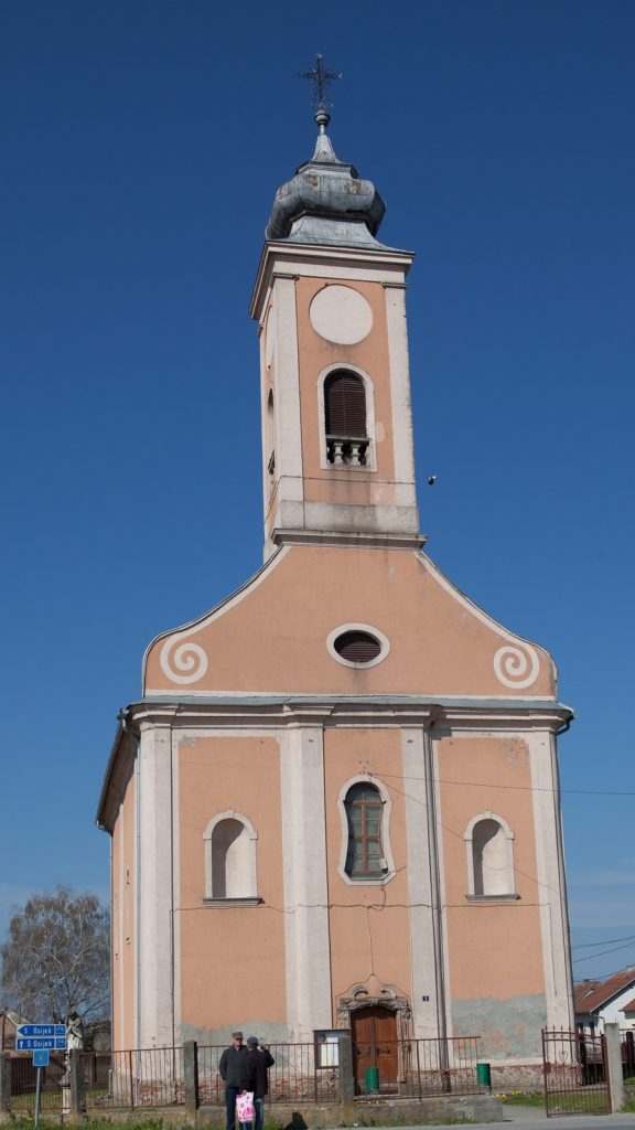Front view of a peach-colored church with a tall bell tower and a blue sky backdrop.