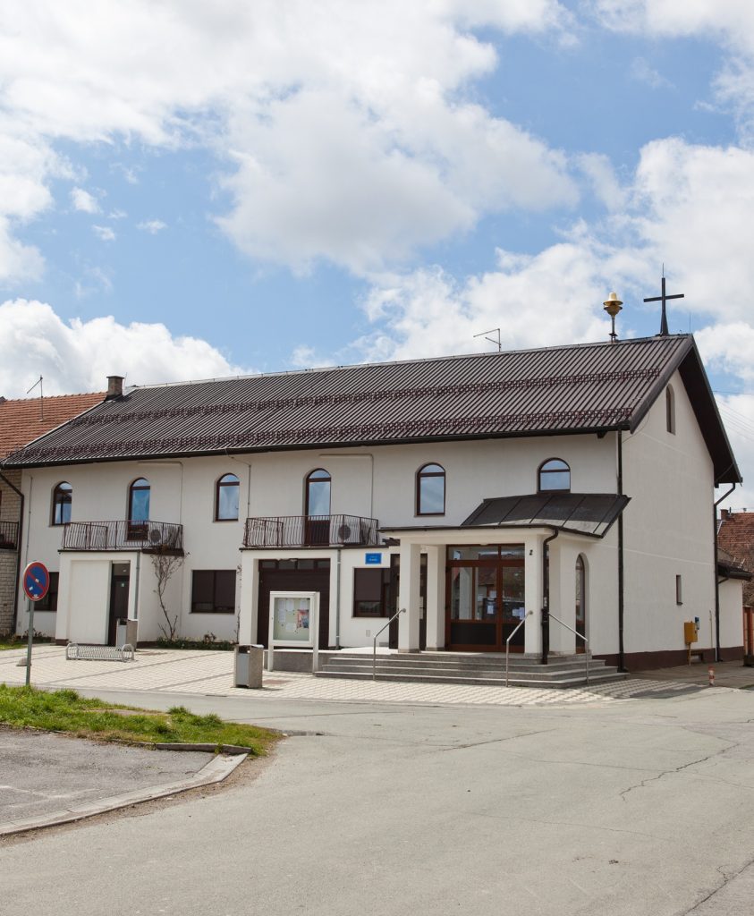 Two-story white building with a dark brown tiled roof and arched windows under a blue sky with clouds.