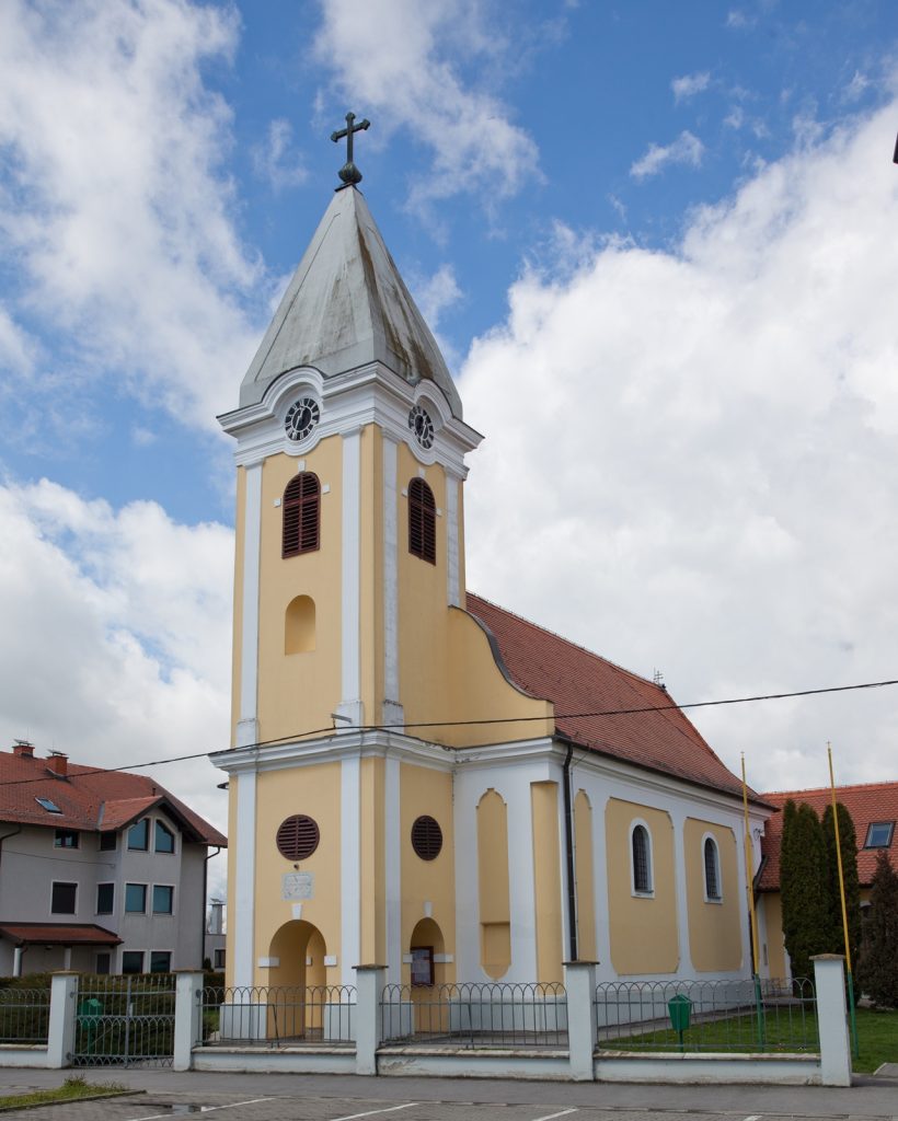Yellow church with a tall steeple and cross above, set against a blue sky with clouds.