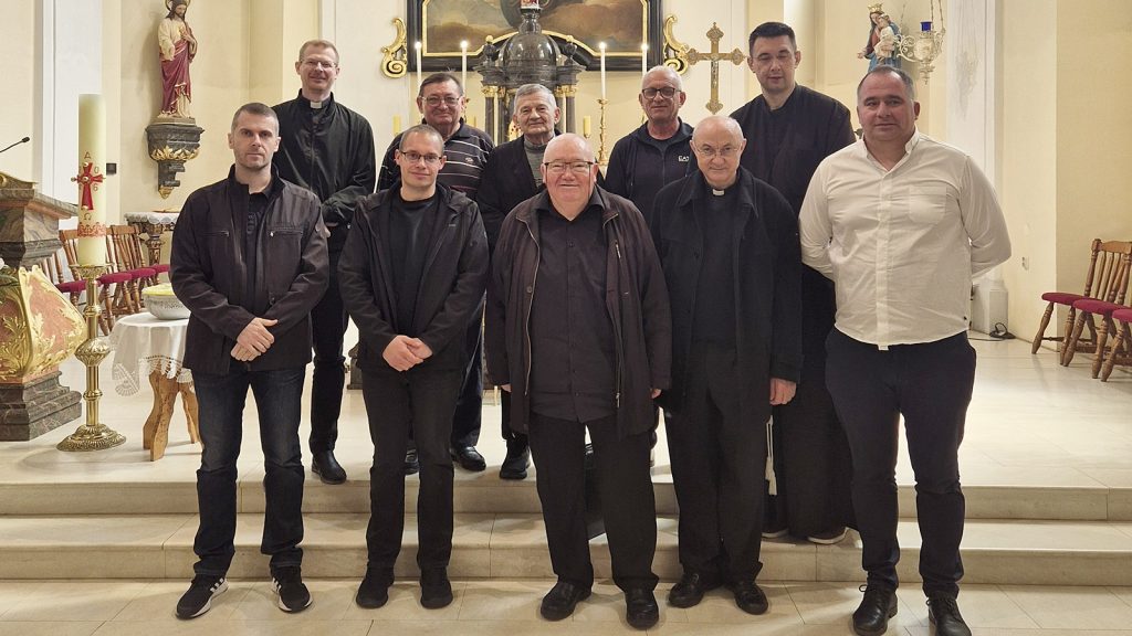 Group of men in dark clothing posing in a church sanctuary with an ornate altar and lit candles behind them.