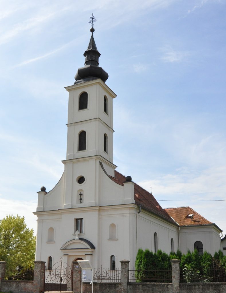 White church with a tall steeple and black onion dome against a blue sky, iron fence in front.