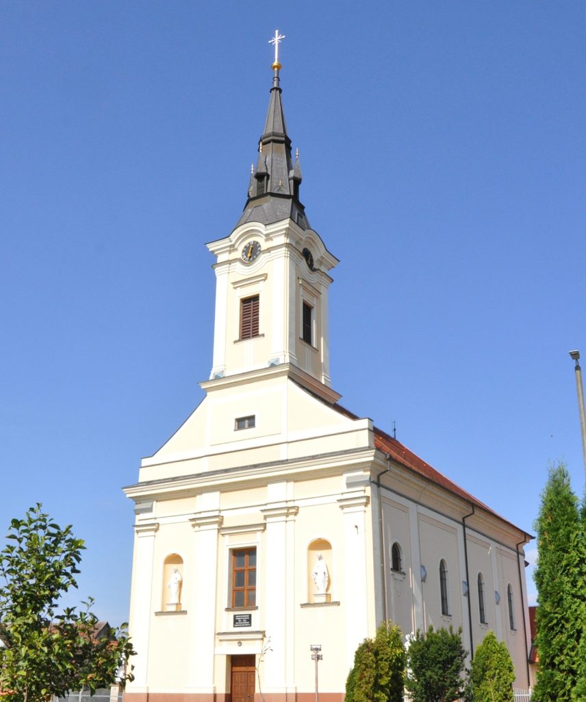 White church with a tall dark steeple and clock faces, set against a clear blue sky.