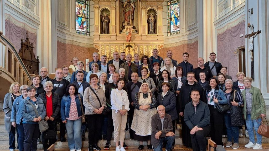 Large group of adults posing for a photo inside a church, with an ornate golden altar and stained-glass windows behind them.