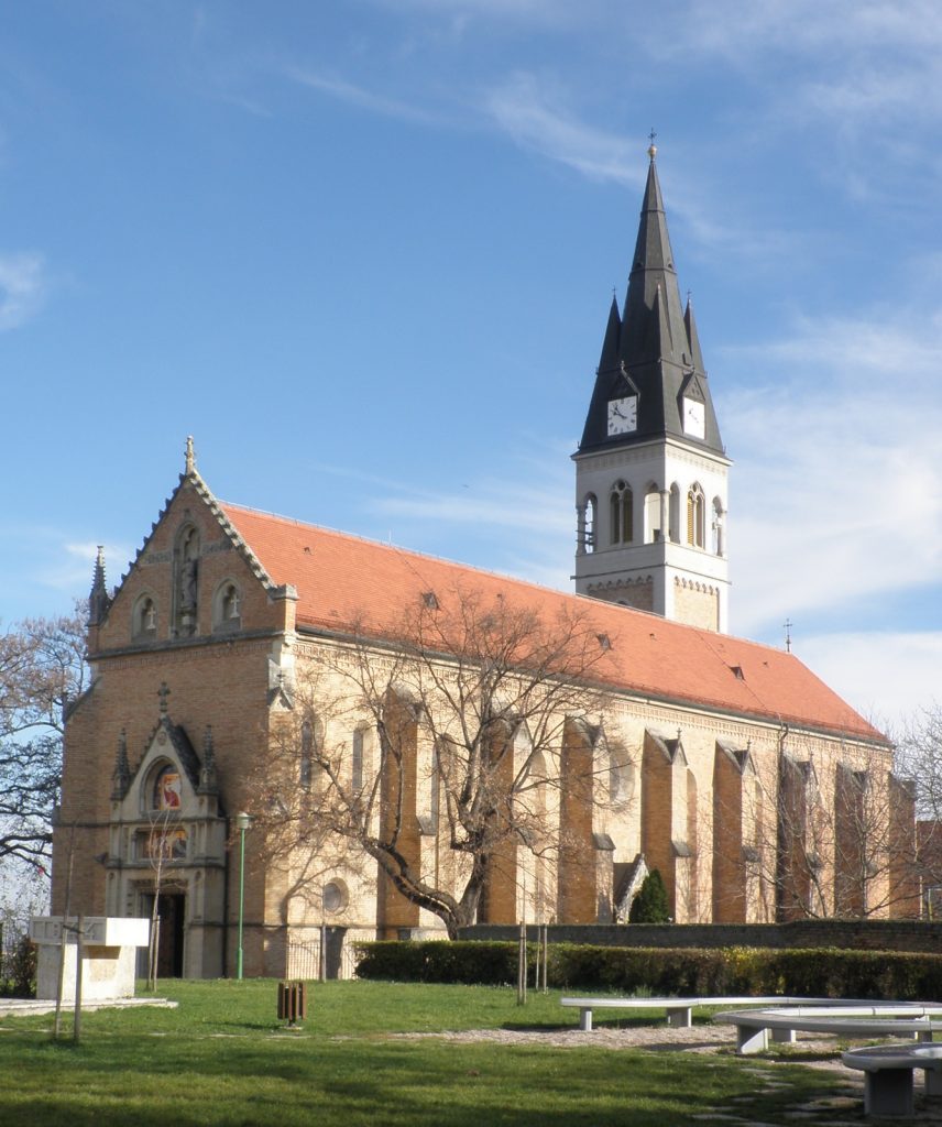 Brick church with a red-tiled roof and a tall clock tower under a blue sky
