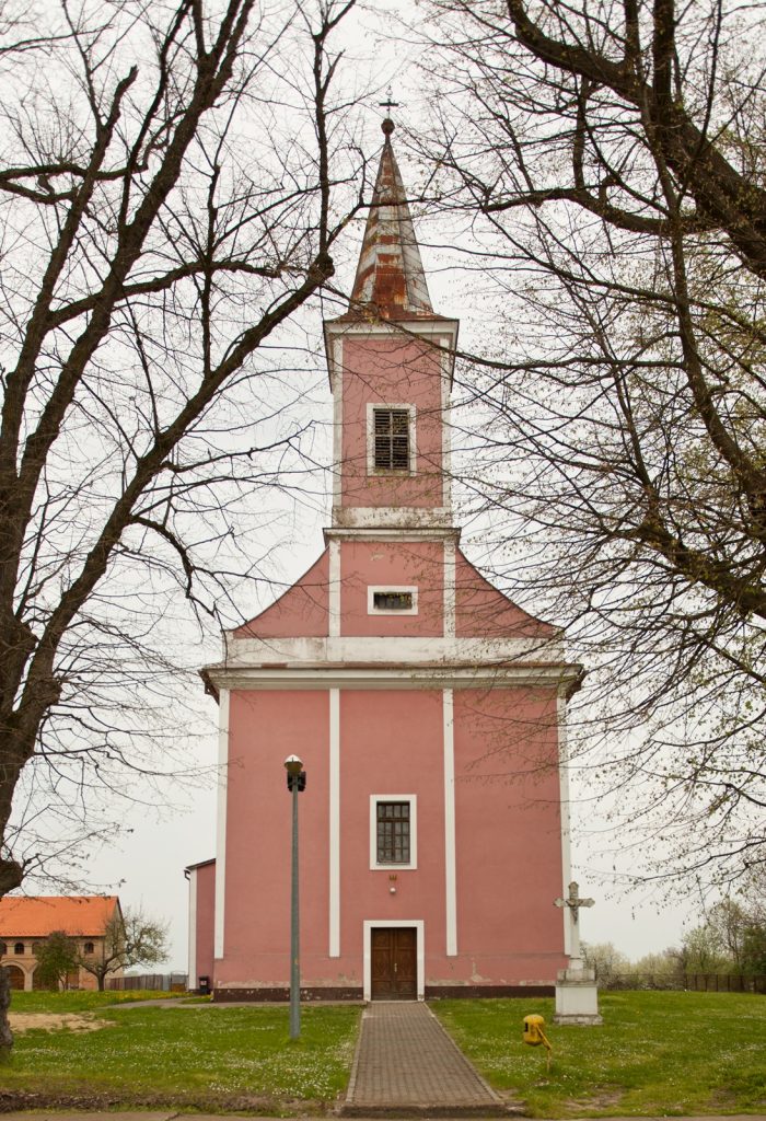 Front view of a pink church with a tall steeple, white trim, surrounded by bare trees and a walkway.