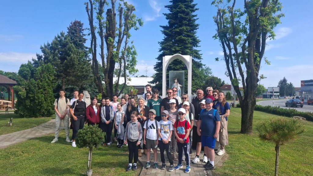 Group photo of students and adults posing together in a park with a white arch statue behind them on a sunny day