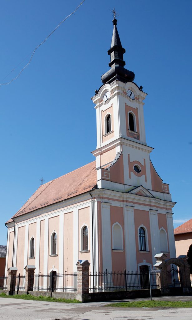 Church with peach facade and tall clock tower against a clear blue sky, arched windows visible along the side