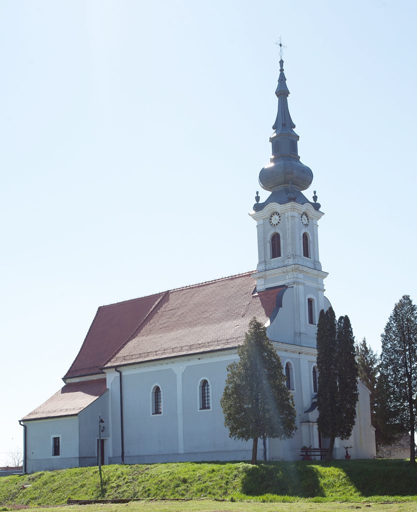 White church with a red-tiled roof and a tall baroque-style steeple against a clear blue sky