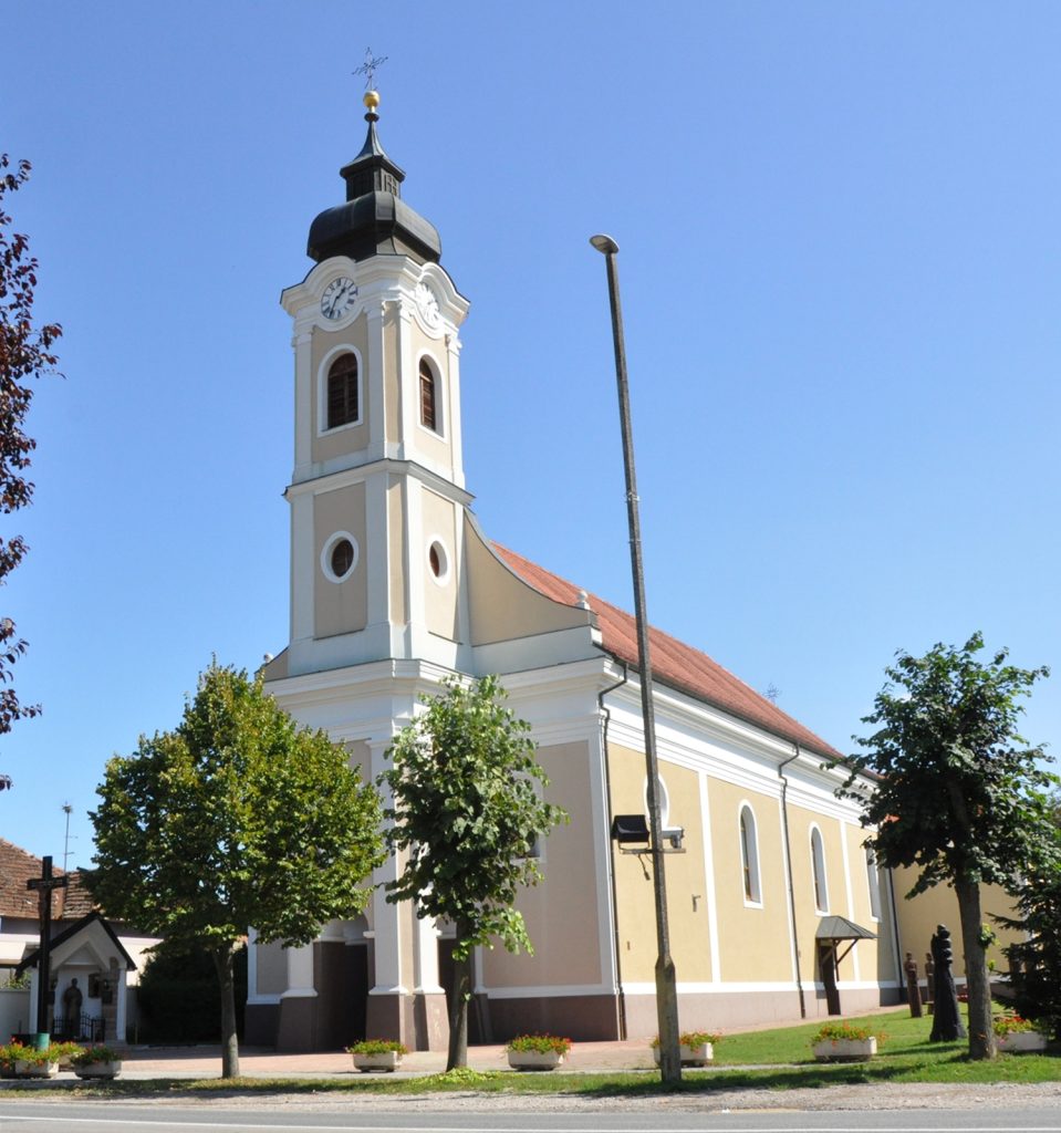 Church with a clock tower and ornate white facade under a clear blue sky, red-tiled roof visible on the side