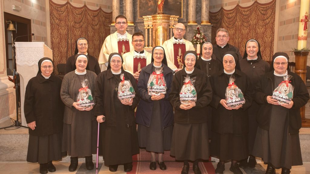 Group of Catholic nuns and priests posing in a church, each nun holding a wrapped gift bag in front of an ornate altar.