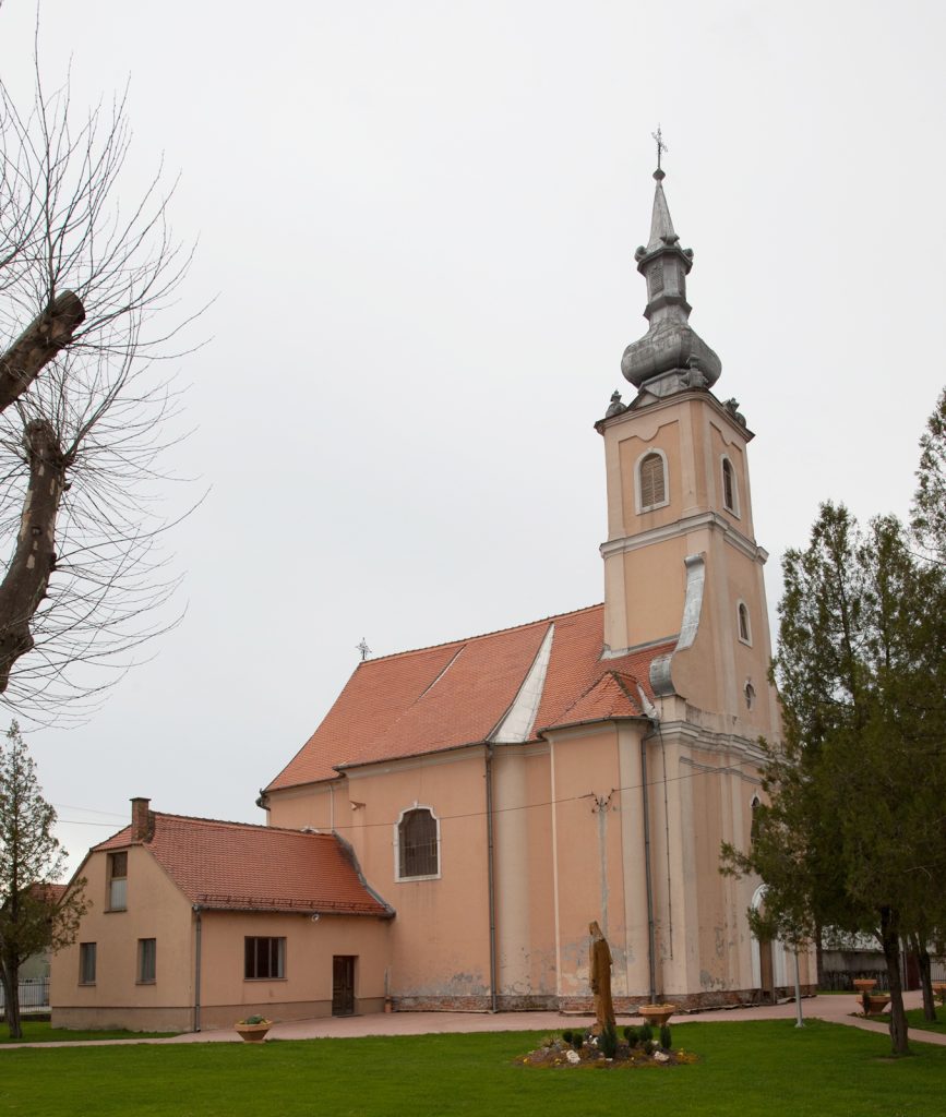 Church with peach-colored walls, red-tiled roof, and a tall ornate steeple topped with a cross