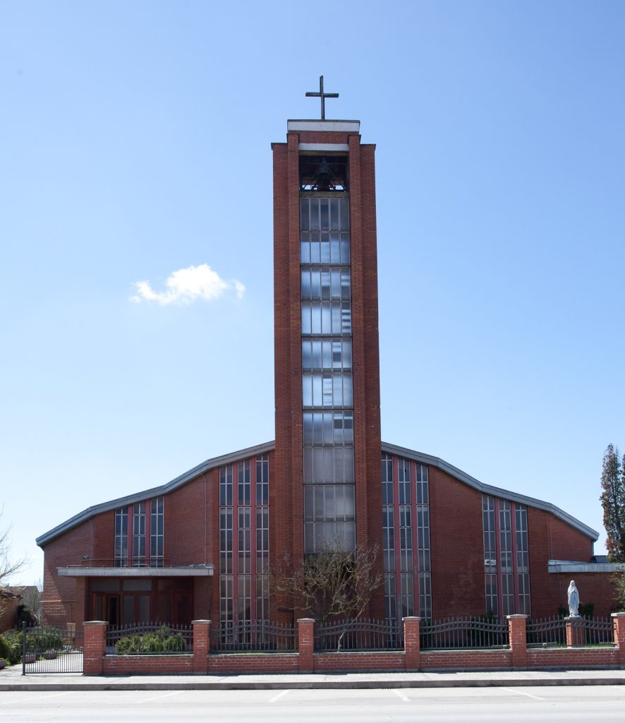 Brick church with a tall central bell tower topped by a cross against a blue sky.