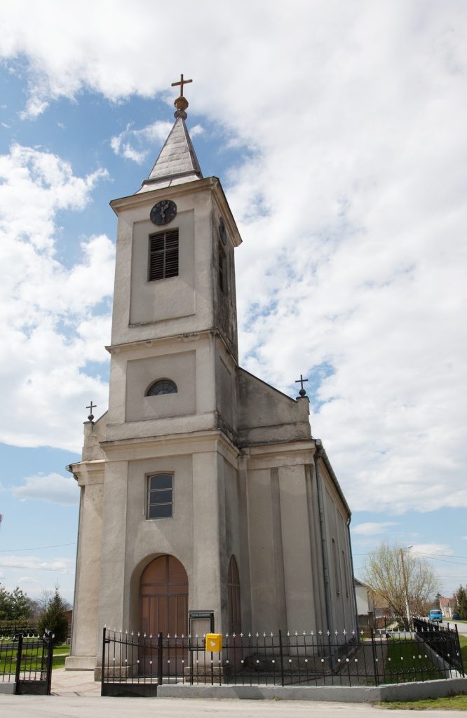 White church with a tall steeple, cross atop, and arched entrance against a blue sky.