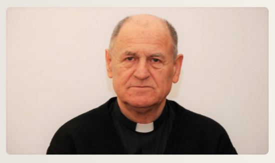 Portrait of an older man wearing a clerical collar, facing the camera with a neutral expression, against a light background.