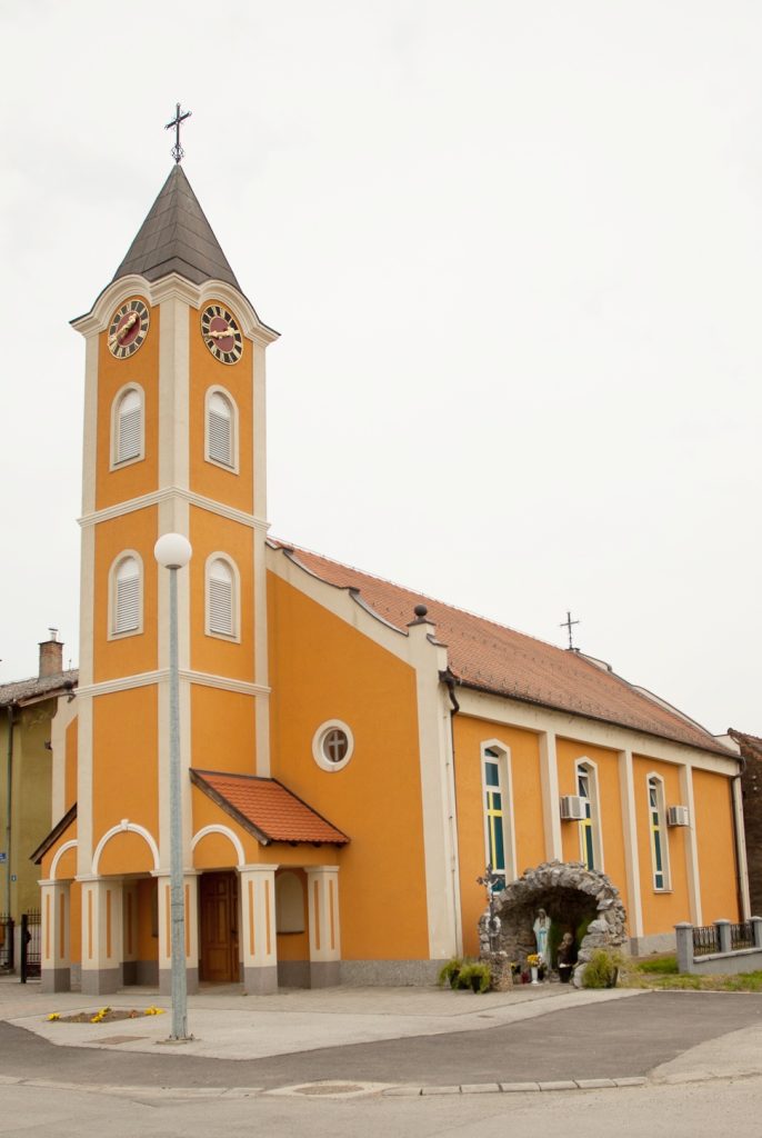 Orange church with a tall clock tower and arched windows in a small town setting.