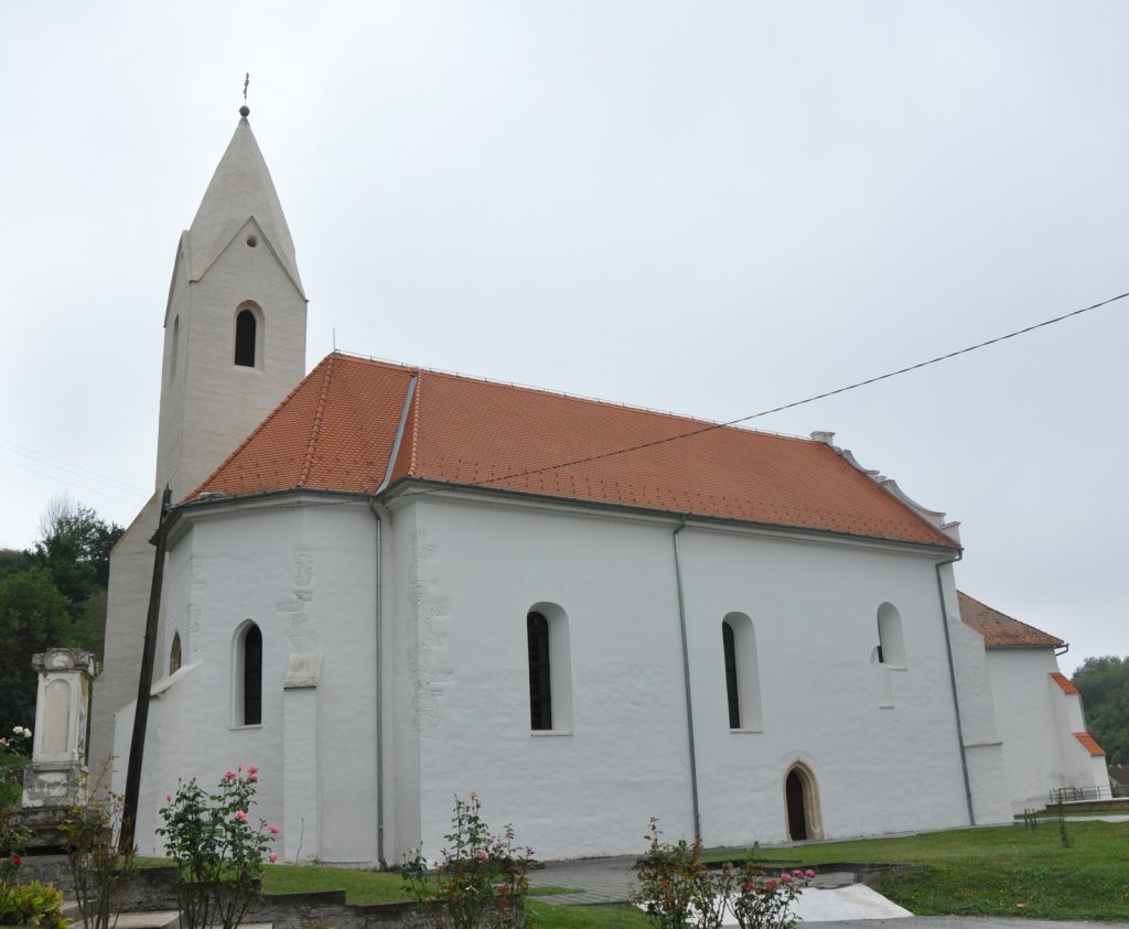 White church with a tall, pointed steeple and red-tiled roof under a gray sky.