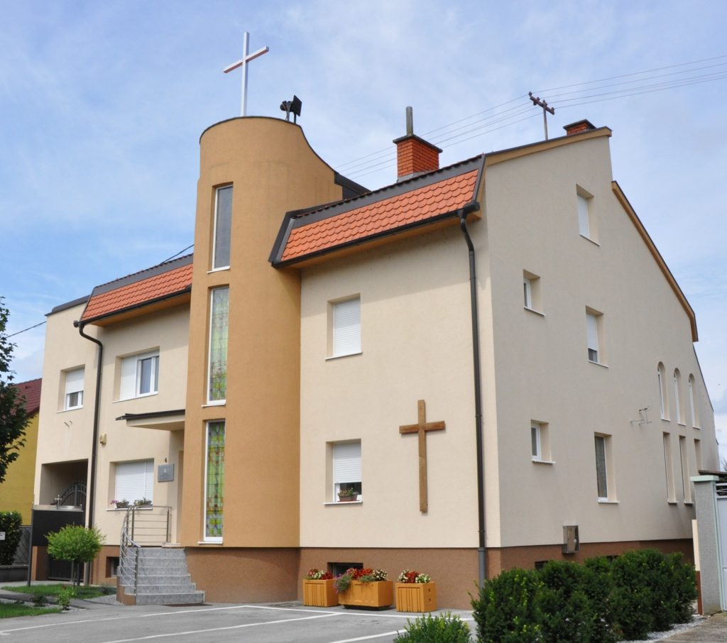 A beige residential building with a church-style tower and a white cross on top against a blue sky.