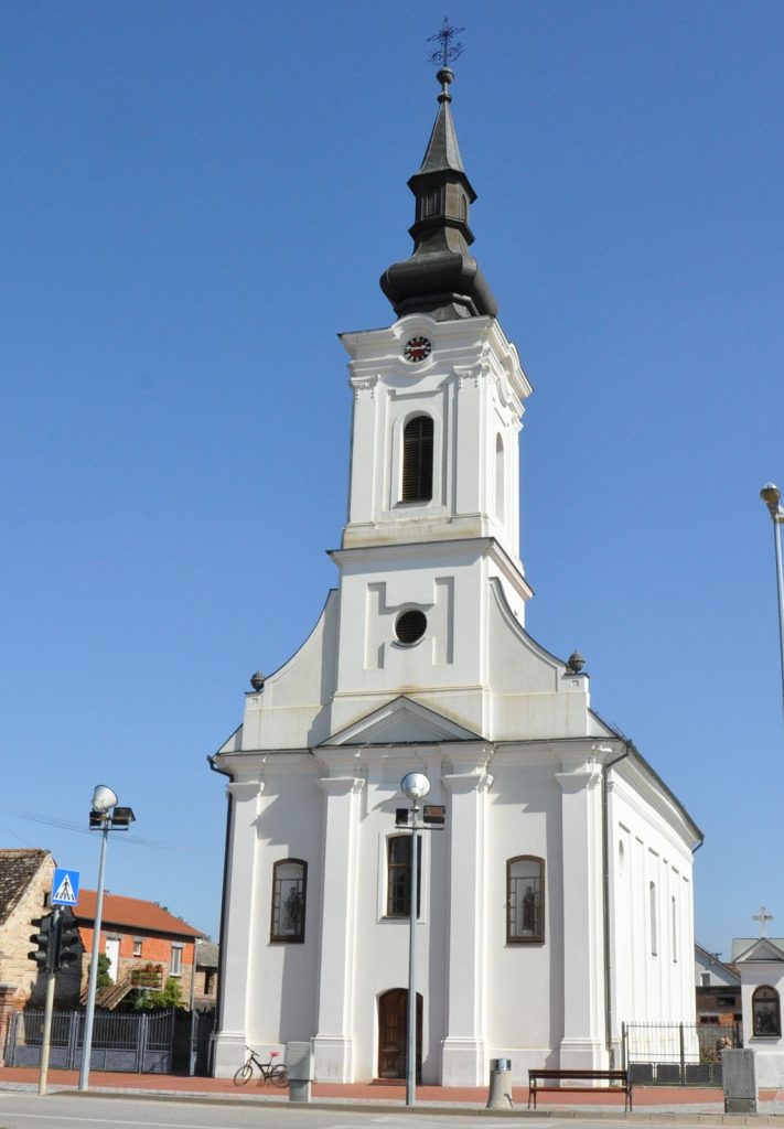 White church with a tall black steeple against a blue sky, clock face visible above the entrance.