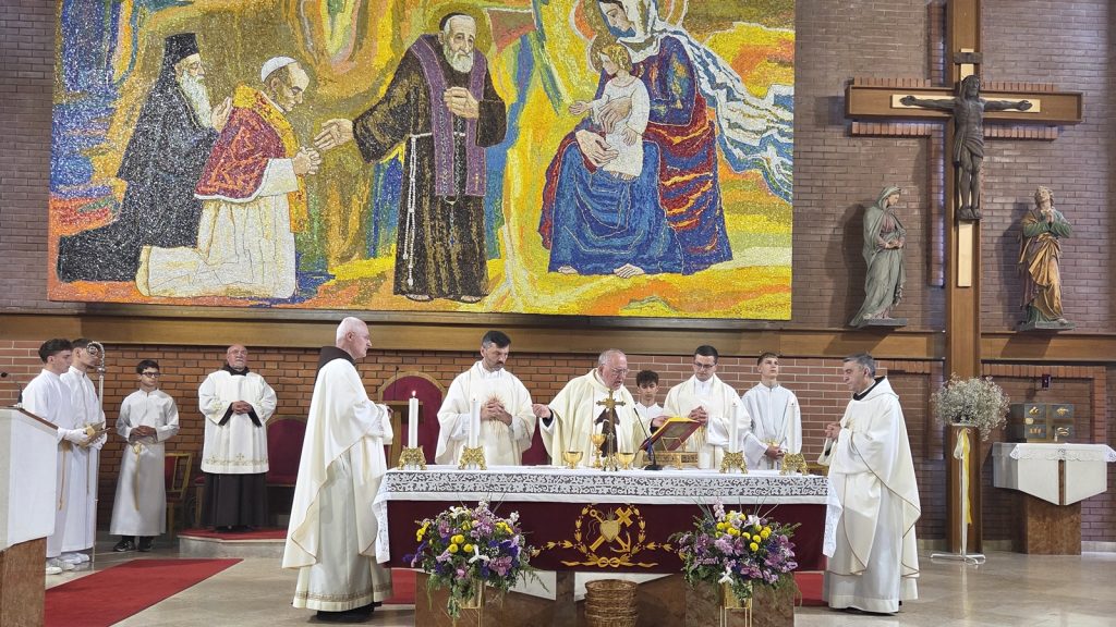 Priests celebrating Mass at an ornate altar in a church, with a large colorful mural and crucifix on the wall behind them.