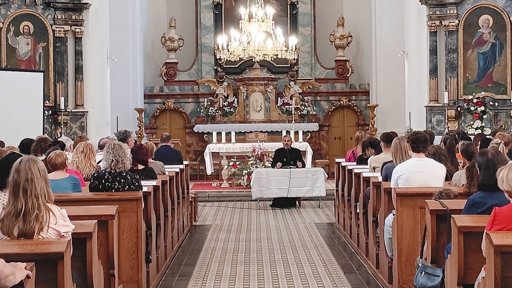Priest at a white-clothed table at the altar addressing a full congregation in an ornate church.