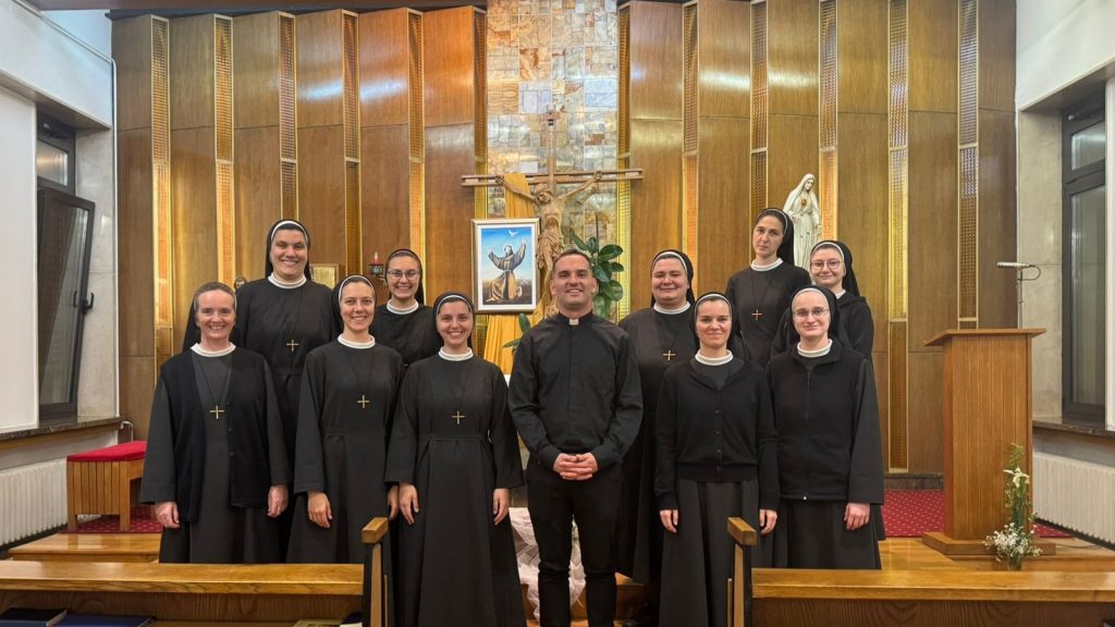 Group of nuns and a priest posing for a photo in a church sanctuary with a crucifix and framed image behind them.