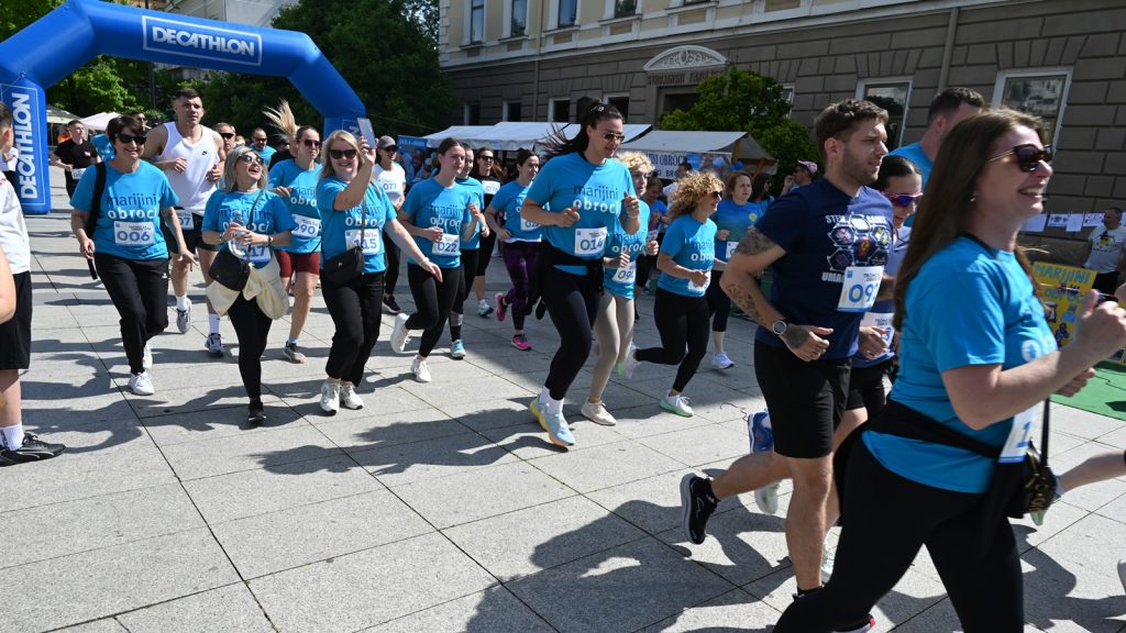Group of runners wearing matching blue shirts starting a race under a blue Decathlon arch on a sunny day.