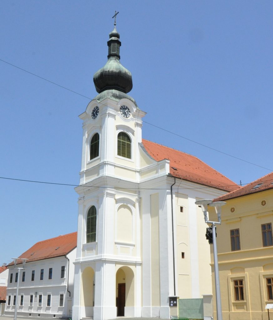 White church with clock tower and a green onion dome reaching into a clear blue sky