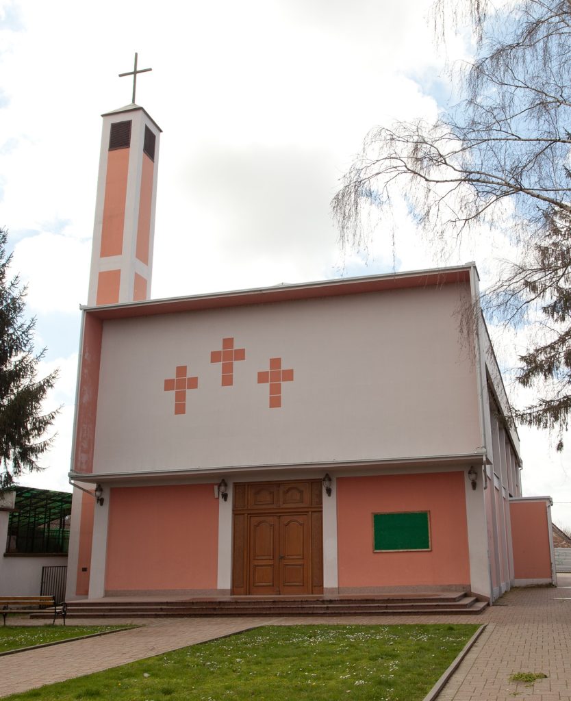 Peach-colored church exterior with a tall cross-topped steeple, and three decorative orange crosses on the facade near the entrance.