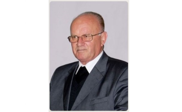 Older man in a gray suit and glasses posing for a formal portrait with a neutral background.
