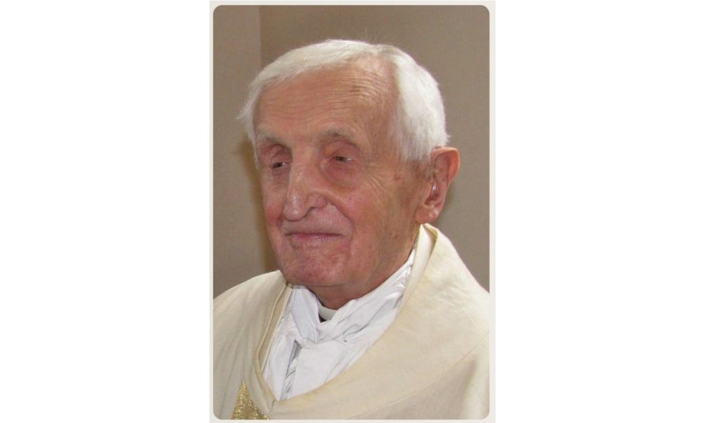 Elderly man with white hair wearing cream liturgical robes, looking ahead with a gentle smile.