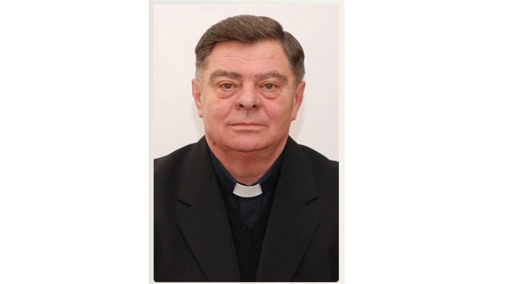 Portrait of a middle-aged priest in a black suit with a white clerical collar, looking at the camera.