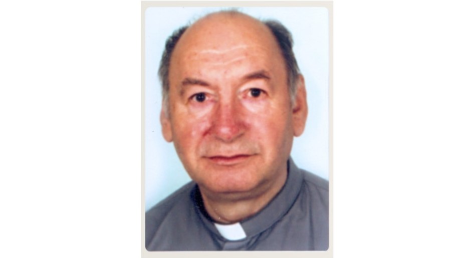 Portrait of an older man in a gray clerical shirt with a white clerical collar against a pale background.
