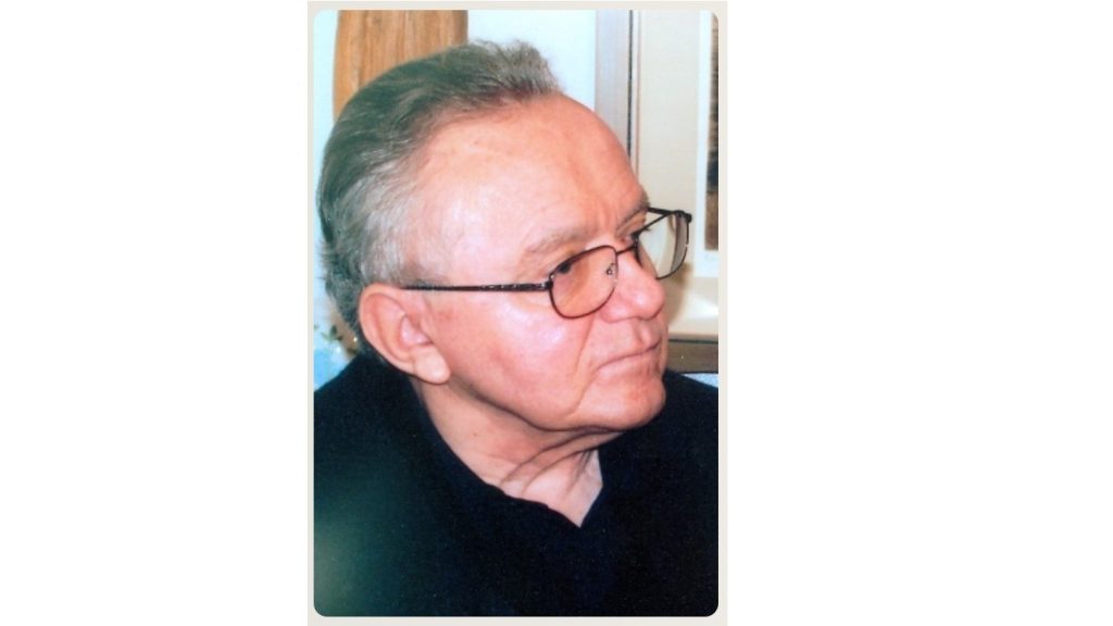 Side profile of an elderly man with gray hair and glasses wearing a dark shirt, looking to the right.