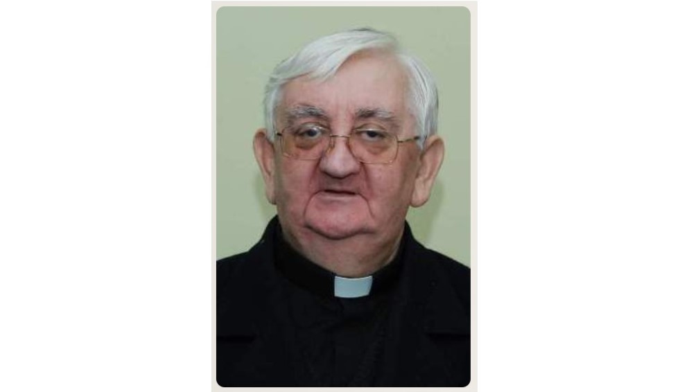 Portrait of an older man wearing a clerical collar and glasses, facing the camera with a neutral expression.