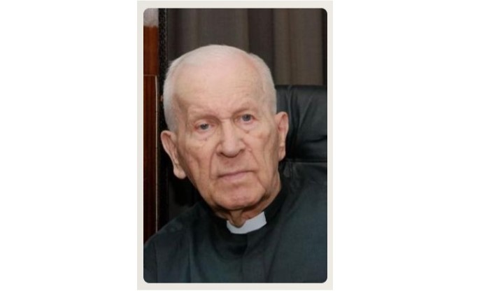 Portrait of an elderly priest with a white clerical collar, looking thoughtful indoors.