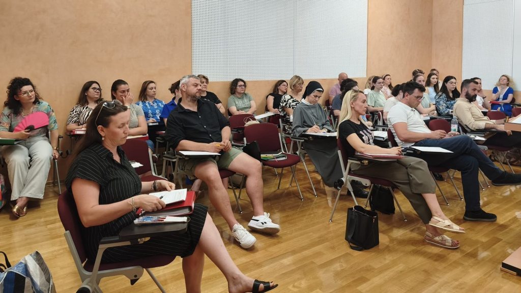 Group of adults seated in a classroom, taking notes during a lecture in a seminar room.
