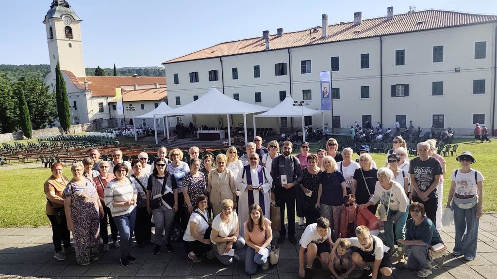 Large group of people posing for a photo on a sunny day in front of a historic building with a clock tower and white event tents outside.
