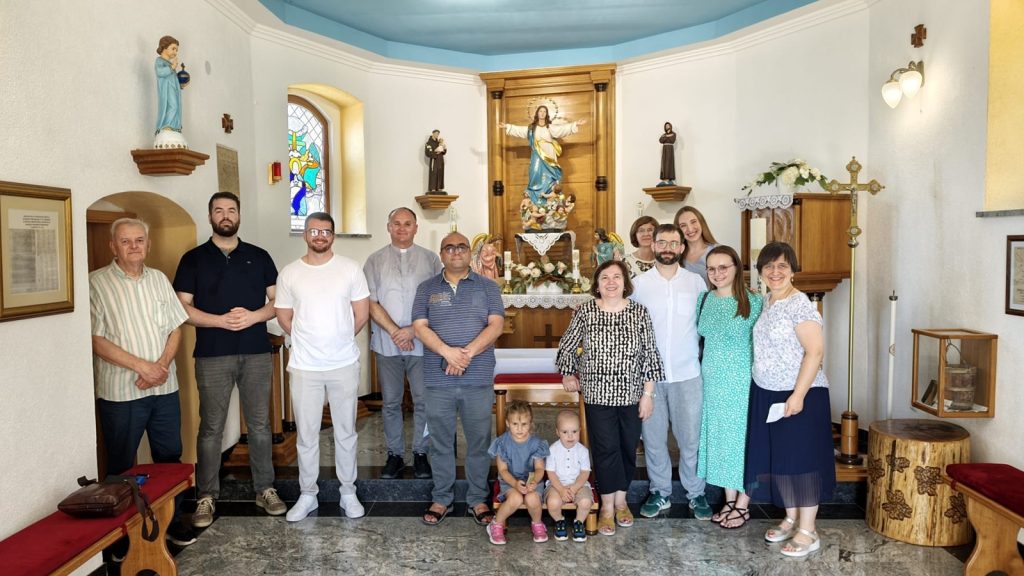 A diverse group of people posing together in a church sanctuary in front of the altar with a Jesus statue and stained glass windows.